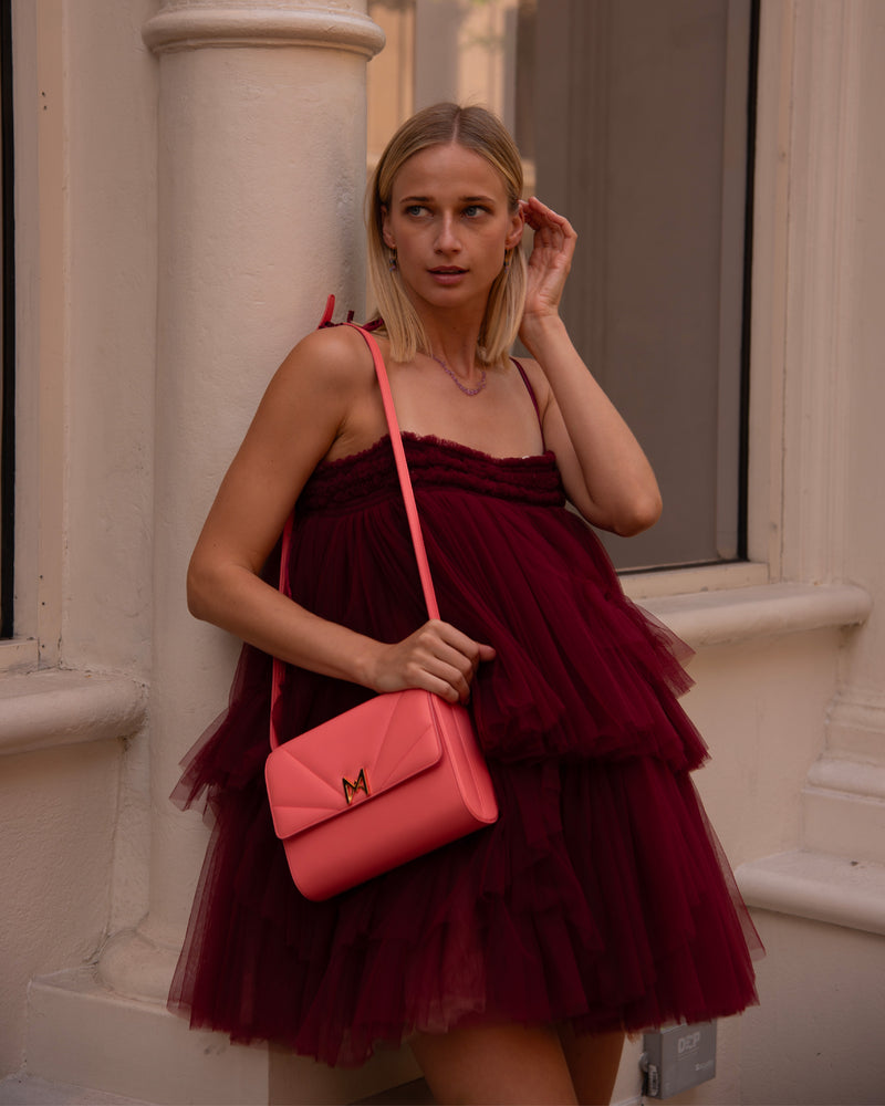 sac à main M1_01 en cuir de veau upcyclé couleur corail , porté par une femme blonde en robe rouge carmin